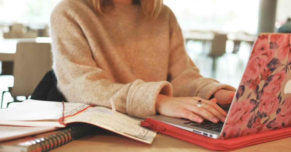 Vrouw aan een tafel met een laptop, een opengeslagen agenda en notitieboeken naast zich